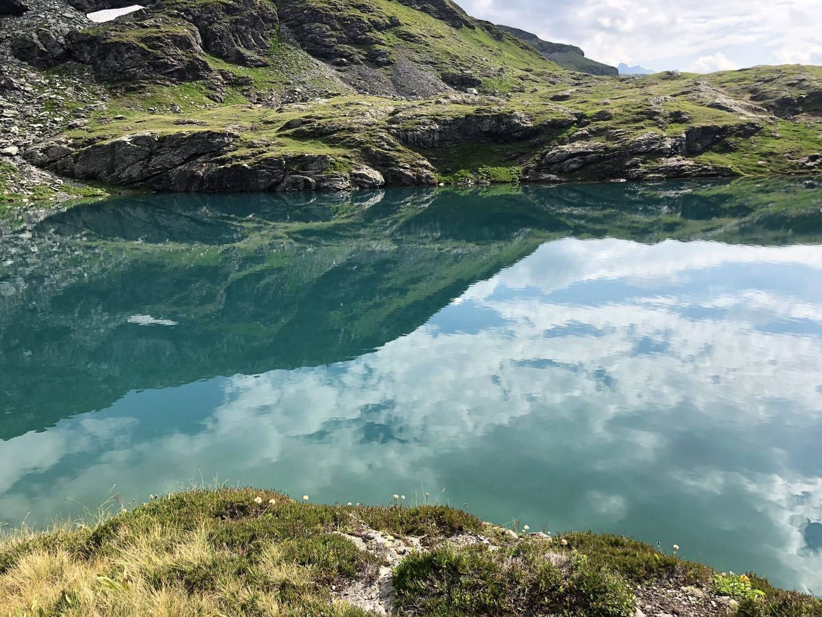 Bergsee, in dem sich Wolken und Gipfel spiegeln
